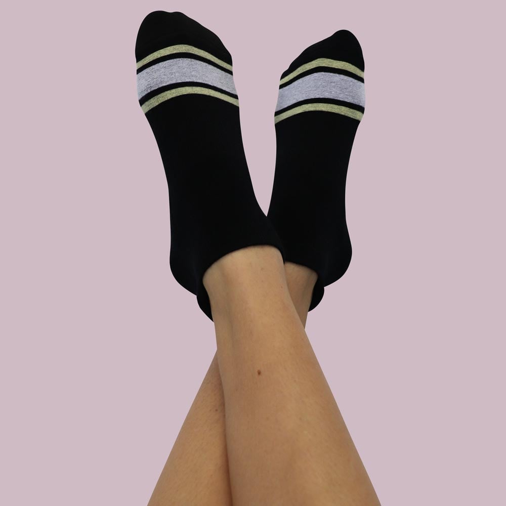 Grip-Socks-BlacknGold-Hoops-short A pair of legs in black socks with white stripes, relaxed and stylish against a neutral backdrop.